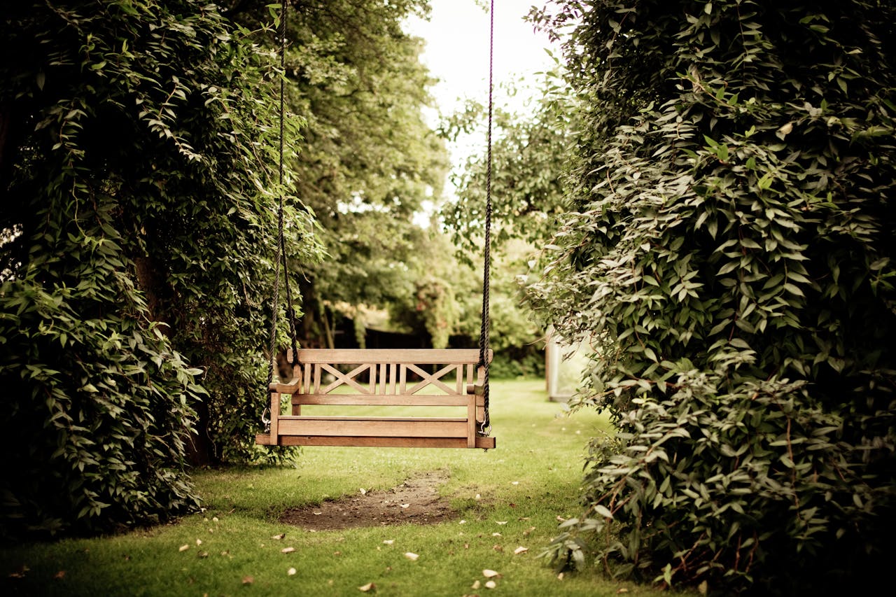 who-we-are A tranquil wooden swing hanging in a verdant garden setting, ideal for relaxation.